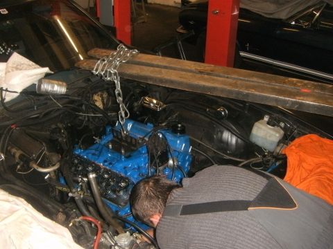 1972 Ford Ranchero - A blue engine is being installed into a vehicle's engine bay with the help of chains and wooden beams.