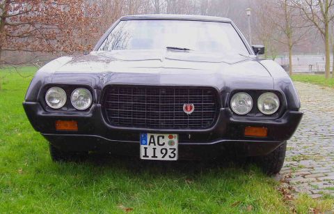 1972 Ford Ranchero - Front view of a black car a prominent grille and dual headlights, parked on grass.