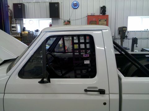 1994 Ford F-150 - A white pickup truck cab is shown from the side, with a roll cage and racing net visible inside the window.