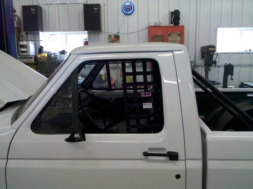 White Ford pickup cab with black window safety net and roll cage in a shop