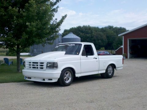 1994 Ford F-150 - This white 1994 Ford F-150 features a prominent hood scoop and drag racing decals, suggesting performance modifications.