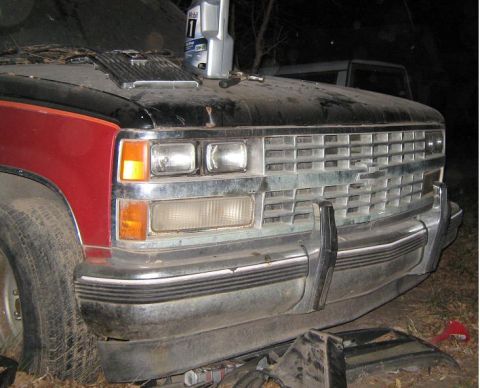 2000 Mercury Grand Marquis - A red and black Chevrolet C/K truck's front grille and headlights are visible, with another vehicle in the background.