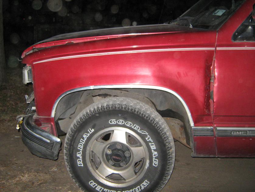 Red GMC pickup truck front fender and wheel, with damage to the door