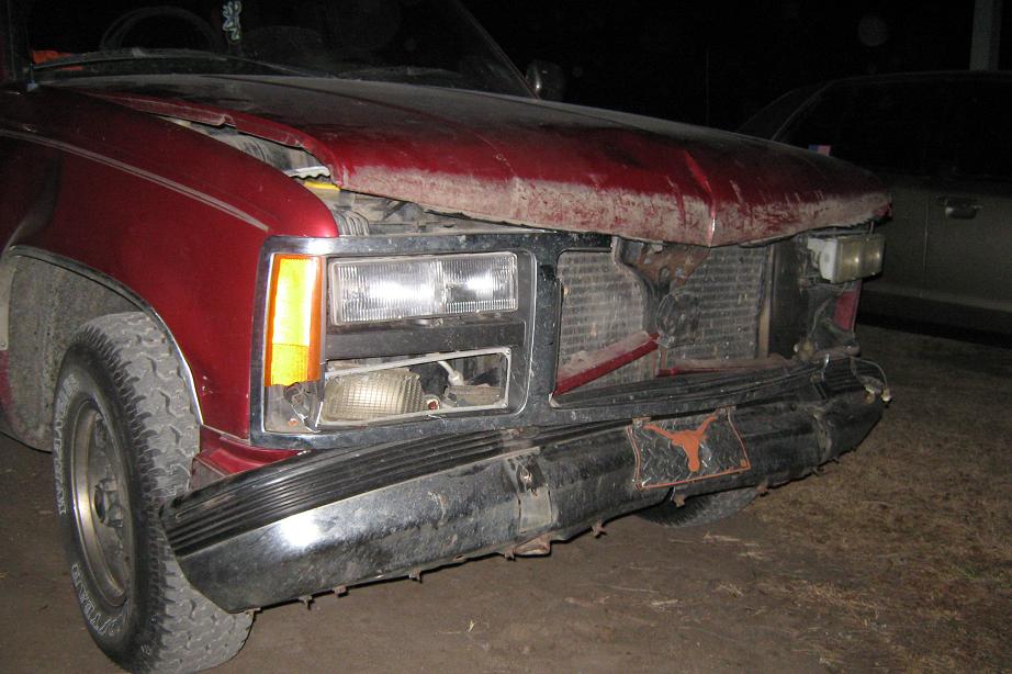 Red pickup truck front end damaged, hood bent, grille exposed