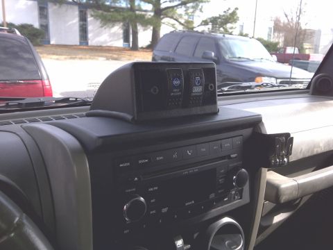 2007 Jeep Wrangler - The dashboard of a Jeep Wrangler features an overhead console with two auxiliary switches and a car stereo below.