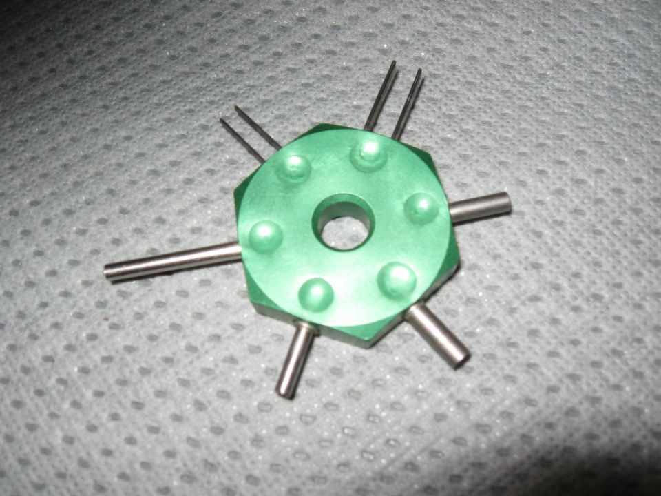 Green automotive tool with six metal pins and a central hole