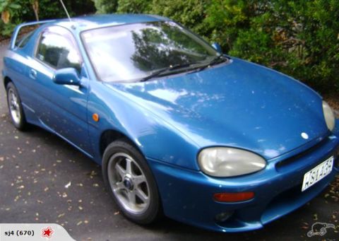 1993 Mazda MX-3 - A blue 1993 Mazda MX-3 coupe is shown from a 3/4 front angle, a distinctive rear spoiler.