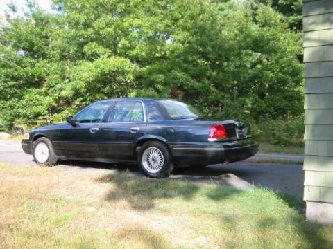 1998 Ford Crown Victoria - A dark green 1998 Ford Crown Victoria sedan is viewed from the side, parked outdoors near a house and trees.
