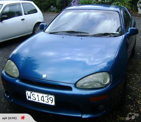1993 Mazda MX-3 - A blue 1993 Mazda MX-3 is parked next to a white car. The front of the coupe is visible.