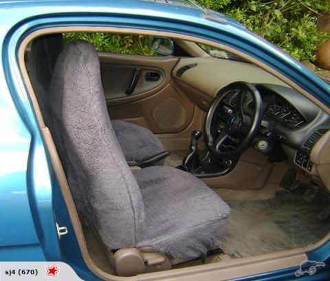 1993 Mazda MX-3 - The interior of a blue car is shown, fuzzy grey seat covers and a tan dashboard.
