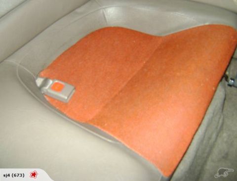 1993 Mazda MX-3 - Close-up of a car's interior, focusing on a seat with an orange fabric insert and a seatbelt buckle.