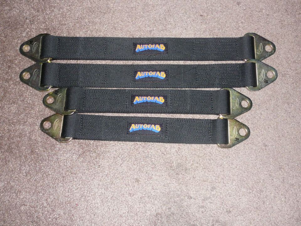 Four black Autofab straps with metal mounting brackets on a carpeted surface