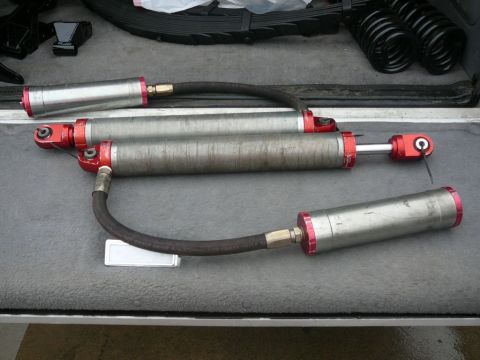 1988 Ford Bronco - Pair of remote reservoir shock absorbers and leaf springs are laid out in the back of a vehicle.