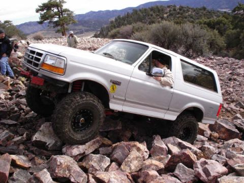 1996 Ford Bronco - A silver Ford Bronco is shown traversing a challenging rocky terrain with a driver visible inside.