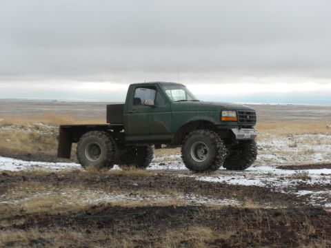 1989 Ford Bronco - Modified 1992 Ford pickup truck with oversized tires and a flatbed, seen in a winter landscape.