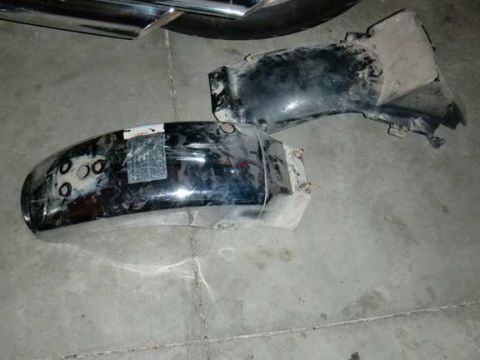 1980 Honda CB750 - Two motorcycle fenders, one chrome and one black, lie on a concrete surface, possibly awaiting installation or repair.