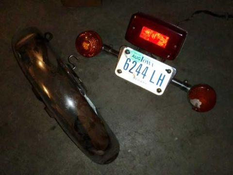 1980 Honda CB750 - A collection of motorcycle parts, including a chrome exhaust and a license plate, are laid out on a concrete surface.