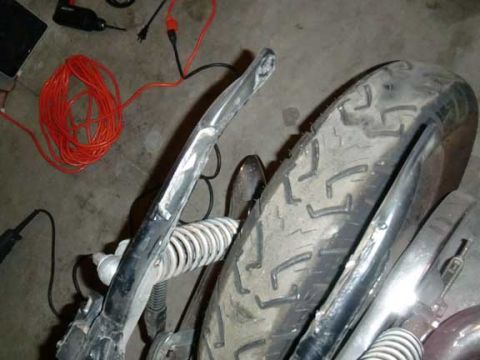 1980 Honda CB750 - Close-up of a motorcycle's rear wheel and suspension, with tools and electrical cords nearby.