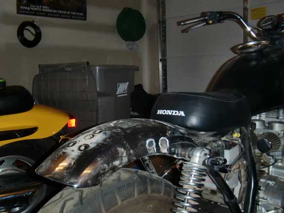 Black Honda motorcycle seat with white lettering, close-up on rear fender and tire