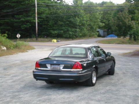 1998 Ford Crown Victoria - Rear view of a dark 1998 Ford Crown Victoria sedan parked on a gravel surface with trees in the background.