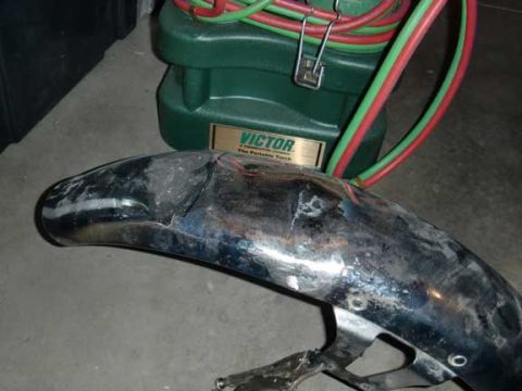 1980 Honda CB750 - A damaged chrome motorcycle fender sits on a concrete floor next to a portable torch kit.