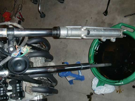 Motorcycle front forks being worked on, with engine components and a drain pan of oil visible