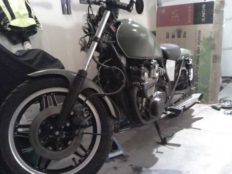 1980 Honda CB750 motorcycle in garage, undergoing rebuild. Front wheel, engine, and fuel tank are visible