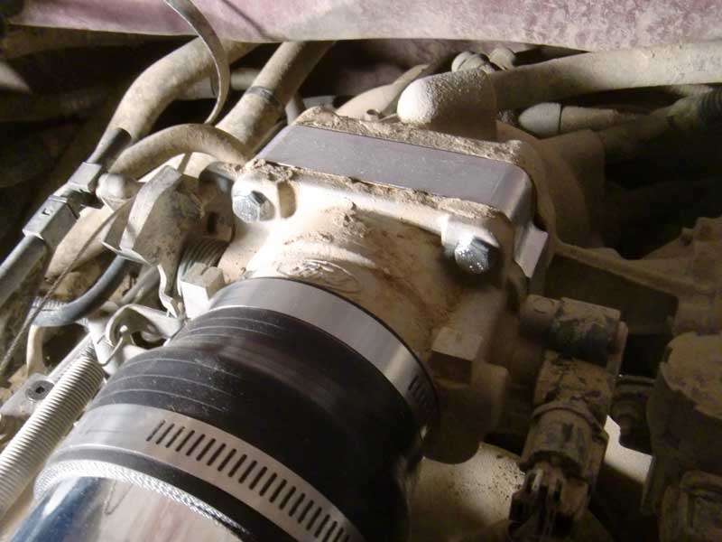 Close-up of a dusty engine part with a silver plate and hose clamp