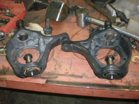 1995 Ford Bronco - Two black suspension knuckles with ball joints are laid out on a workbench, possibly for repair or replacement.