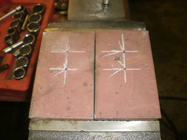 Two metal plates marked with chalk lines and drill points, held in a vise. A red toolbox with sockets is to the left