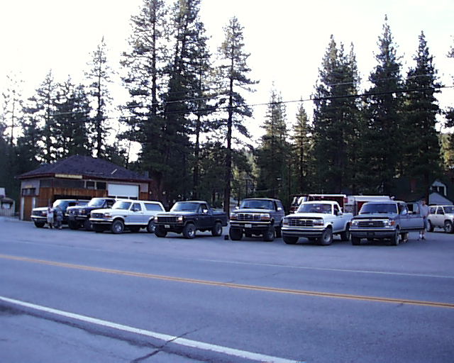 Several pickup trucks and one SUV parked in front of a building with trees behind them