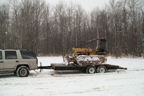 1963 Hummer H3 - A yellow bulldozer is transported on a trailer by a white SUV during a snowfall.