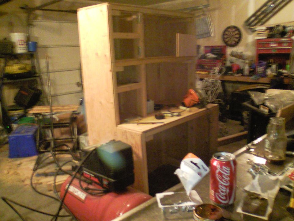 Garage scene with unfinished wooden cabinet, air compressor, and Coca-Cola can