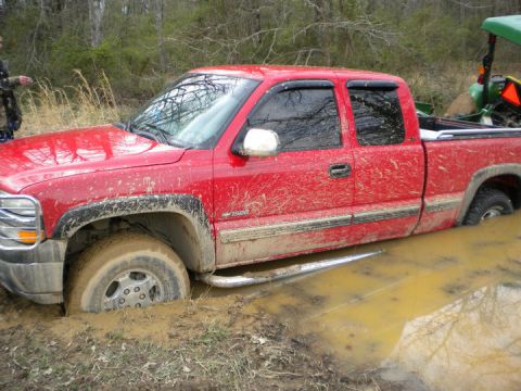 1989 Ford Bronco - Red pickup truck stuck in mud, with a tractor visible in the background.