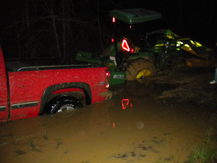 red pickup truck stuck in mud next to a green tractor