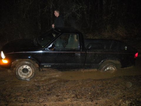 1989 Ford Bronco - A black pickup truck is stuck in deep mud at night, with a person standing nearby.