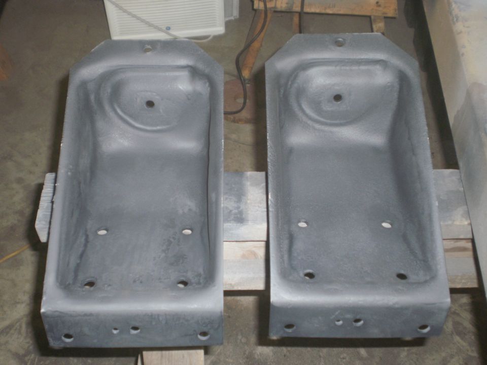 Two gray metal brackets with multiple mounting holes, resting on wooden planks