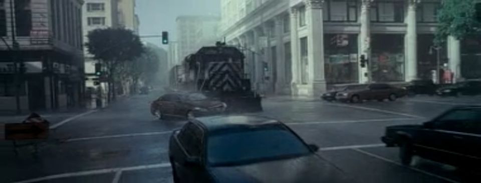 Train passing through a city intersection on a rainy day, with several cars on the wet street