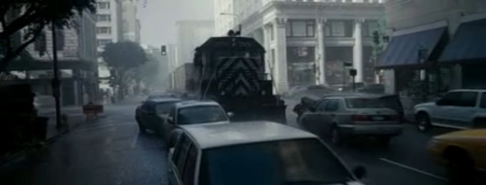 Train and multiple cars on a wet city street with buildings on either side