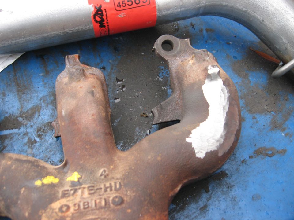 Rusty cast-iron exhaust manifold with weld repair, marked E7TE-HD, on blue surface
