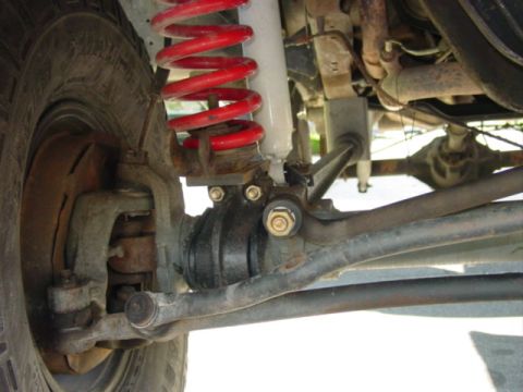 1990 Ford Bronco - Close-up underside view of a Ford Bronco's front suspension showing a bright red coil spring and shock, a black rubber ball-joint/boot, tie…
