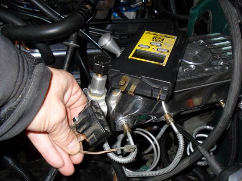 1990 Ford Bronco - A hand holds a black trapezoidal diagnostic test connector while a yellow-and-black Ford code reader with an LCD screen rests on a polished…