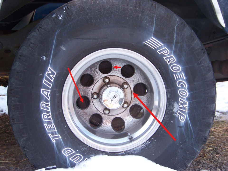 Pro Comp Mud Terrain tire on eight-hole aluminum wheel with red annotation arrows on hub