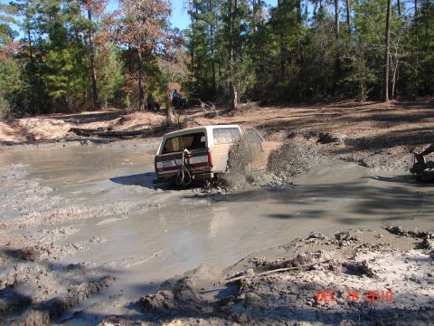 1987 Ford Bronco - A 1987 Ford Bronco navigates a challenging mud pit, kicking up a significant splash.
