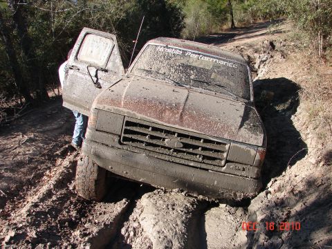 1987 Ford Bronco - This SUV is stuck deep in the mud, with its driver's side door open and a person partially visible inside.