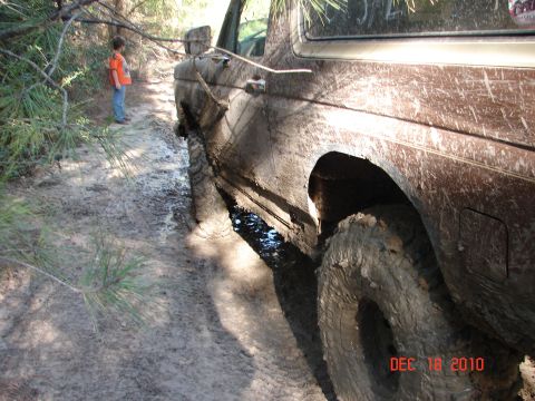 1987 Ford Bronco - Muddy 1987 Ford Bronco stuck on a dirt track with a child observing.