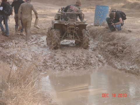 1987 Ford Bronco - An ATV is stuck in a muddy puddle with several people nearby, some covered in mud.