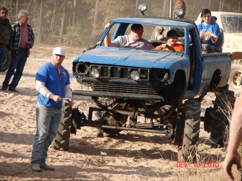 1987 Ford Bronco - A heavily modified blue pickup truck with large tires is shown with several people around it.