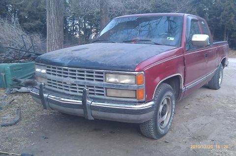 2000 Mercury Grand Marquis - A red pickup truck with a dark hood is parked on a dirt surface, with trees in the background.