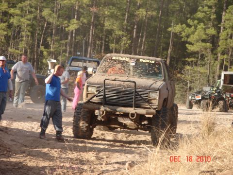 1987 Ford Bronco - A group of people and several off-road vehicles are gathered in a wooded area on a sunny day.